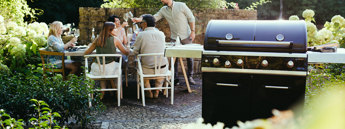 Outdoorchef Dualchef 425 G BZ ψησταριά υγραερίου σε κήπο δίπλα σε τραπέζι με φίλους που απολαμβάνουν BBQ